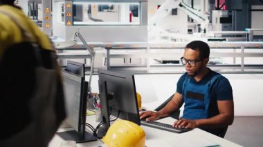 Afrika kökenli Amerikalı mühendis, bir güneş paneli imalat fabrikasında çalışarak, masaüstündeki güneş enerjisi makinelerinden veri topluyor. Otomatik yenilenebilir enerji üretim hattında erkek teknisyen. Kamera B.