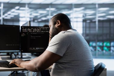 Yorgun mühendis sunucu merkezindeki bilgisayarda yazarken uyuyakalıyor, veri merkezi enerji tüketimini izliyor. Sırt çantalarını incelerken uyanık kalmaya çalışan uykulu bir çalışan.