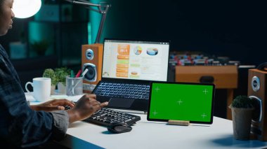 Evde çalışan girişimci, not yazmak için yeşil ekran aygıtı kullanıyor. Kişisel apartman ofisindeki uzaktan çalışan dizüstü bilgisayar kullanarak, model tabletindeki önemli bilgileri kopyalıyor