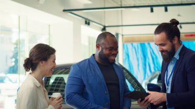 Showroom temsilcisi araba satışına eşlik eden evrakları tamamlar, müşterilerle el sıkışır ve araba anahtarı teklif eder. Satış elemanı müşterilerle sözleşme imzaladı, anlaşmaya vardı, kamera A