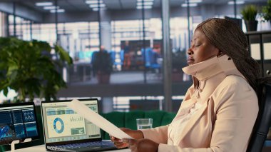 Servikal tasmalı CEO aylık raporlara göre çalışanların performanslarını değerlendiriyor, yaralanmadan sonra tıbbi boyun köpüğünü giyerken genel analizler yapıyor. Yönetmen trendleri inceliyor. Kamera A.