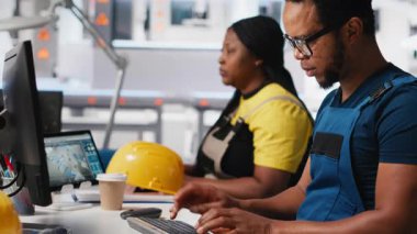 Çalışanlar, yüksek teknolojili sürdürülebilir bir tesiste güneş enerjisi fabrikasında robotik silahları kontrol etmek için bilgisayar kullanıyorlar. Teknisyen otomasyon ayarlarını tutarlı üretimi destekleyecek şekilde ayarlar. Kamera A.