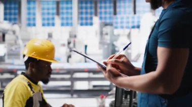 Siyah fotovoltaik fabrikası teknisyeni evrakları inceliyor, üretim verilerini analiz ediyor. Güneş panelleri, sorun çıkarmak için dosya okuyan fabrika işçisi üretiyor. Kamera A.