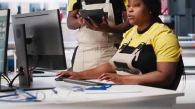 Siyahi çalışanlar fotovoltaik fabrikasındaki güneş panellerini analiz ediyor, verileri analiz ediyorlar. Fabrika mühendisleri, sorun çözme hataları için döküman dosyaları okuyorlar. Kamera A.
