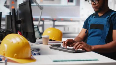 Siyah mühendis güneş paneli montaj yazılımında tanısal kontroller yaparak üretim sürecini ve güneş pillerini alternatif enerji için optimize ediyor. Yüksek teknoloji modern fabrika. Kamera A.