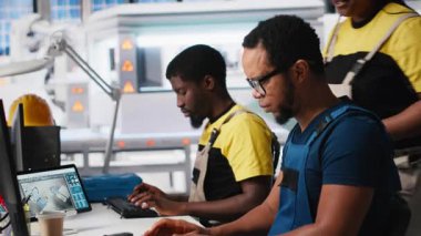 Siyah teknisyenler gelişmiş endüstriyel yazılımlar kullanarak güneş enerjisi tesisinde bilgisayar ayarları üzerinde çalışıyorlar. Otomatik montaj için iş arkadaşları güneş paneli sistemlerini zorluyor. Kamera A.