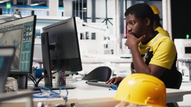 Erkek uzman makine parametrelerini güneş paneli üretimi için ayarlıyor, yüksek teknoloji üretim tesisinde çalışıyor. Siyah mühendis bilgisayarda teknik verileri analiz ediyor. Kamera B.