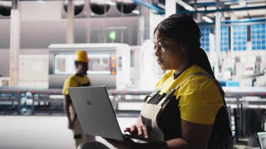 Fotovoltaik fabrikasındaki kadın mühendis arızalı sistemleri tespit etmek için dizüstü bilgisayarda izleme yazılımı kullanıyor. Güneş panelleri fabrika işçisi üretiyor. Çalışma saatlerini azaltıyor. Kamera B.