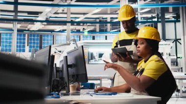 Siyahi çalışanlar fotovoltaik fabrikasındaki güneş panellerini analiz ediyor, verileri analiz ediyorlar. Fabrika mühendisleri, sorun çözme hataları için döküman dosyaları okuyorlar. Kamera B.