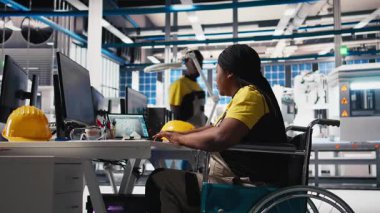 Fotovoltaik fabrikası mühendisi tekerlekli sandalye kullanıcısı endüstriyel bir yazılımda güneş panellerini geliştiriyor, imalat endüstrisinde bilgisayar üzerinde çalışıyor. Yenilenebilir enerji. Kamera B.