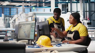 Fotovoltaik fabrikasındaki mühendis ekibi arızalı sistemleri tanımlama yönergelerini inceliyor. Güneş panelleri personeli, operasyonel verimlilik için denetim veri dosyalarını okuyor. Kamera A.