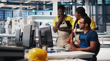 Meslektaşları sürdürülebilir bir endüstriyel fabrikadaki bilgisayar istasyonundan güneş enerjisi teçhizatı alıyor. Siyah mühendislik ekibi CAD yazılım ayarlamalarıyla ilgileniyor. Kamera B.