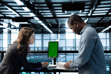 Sunucu odasını model cihazıyla denetleyen bir kadın. Belge evraklarını okuyan, sorun çıkaran bir donanım. Sunucu merkezinde teftiş yapan denetleyici, yeşil ekran tableti hakkındaki teknik dosyaları okuyor