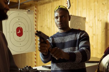 Adam atış poligonunda arkadaşlarıyla vakit geçiriyor, silah doldururken sohbet ediyor ve silah kullanmaya hazırlanıyor. Afrikalı Amerikalı iş arkadaşlarıyla konuşuyor, hedefleri silahla vurmaya hazırlanıyor.