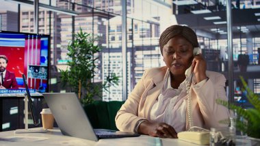 Afrika kökenli Amerikalı yönetmen, mali değerlendirme için sabit telefon görüşmesini kullanıyor. Kadın CEO kaynak tahsisi, bütçe planlaması ve son teslim tarihi yönetimi, karar verme konularını tartışıyor. Kamera B.