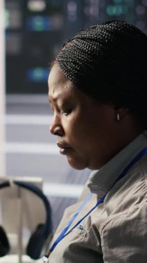 Nöro ağ görselleştirmesini izlemek için PC kullanan dikey video veri merkezi sistem yöneticisiName Sunucu odasındaki Afrikalı Amerikalı kadın, bilgisayar kullanarak donanım öğrenme makinelerini denetliyor.