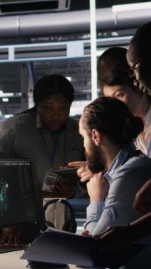 Sunucu merkezinde beyin fırtınası yapan dikey video yöneticileri, makine öğrenme kodlarını ve LLM görselleştirme panellerini gözden geçiriyorlar. Yapay zeka altyapısını izlemek için bilgisayar kullanan veri merkezi bilişim uzmanları