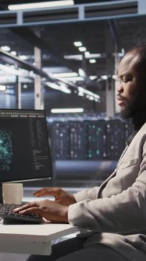 Tüm bilgisayar hatalarını çözdükten sonra sevinen dikey video veri merkezi yazılım geliştiricisi. Sunucu merkezindeki gülümseyen Afrikalı Amerikalı adam PC 'deki görevleri tamamladıktan sonra memnun oldu, sunucu donanımlarını denetliyor.