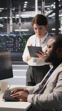 Dikey video sunucu odası yöneticisi, derin öğrenme algoritmalarını inceleyen teknisyeni denetlemektedir. Veri Merkezi Ekip Lideri ve Afrikalı Amerikalı çalışan Yapay Zeka ekipman platformlarının performans gösterge panellerini gözden geçiriyor