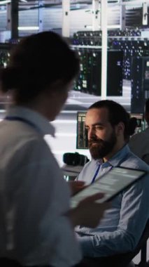 Yapay zeka yazılım güncellemeleri yaparken iş arkadaşıyla konuşan dikey video veri merkezi teknisyeni. Sunucu odası bilişim uzmanı ve iş arkadaşı sohbet ediyor, altyapıyı yapay olarak optimize ediyor