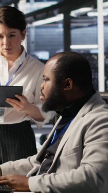 Dikey video sunucu odası yöneticisi, derin öğrenme algoritmalarını inceleyen teknisyeni denetlemektedir. Veri Merkezi Ekip Lideri ve Afrikalı Amerikalı çalışan Yapay Zeka ekipman platformlarının performans gösterge panellerini gözden geçiriyor