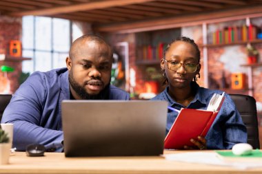 Afrika kökenli Amerikalı bir kadın partneriyle görevleri çözmek için not defterinde raporları kontrol ediyor, evlerinin rahatlığından bağımsız işler yapıyor. Bilgisayarla araştırma yapan odaklanmış insanlar..