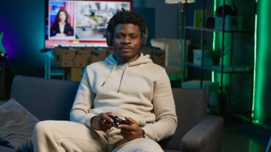 Afrika kökenli Amerikalı bir adam çatı katında video oyunu oynuyor, eğlence olsun diye kontrol cihazını tutuyor. Erkek oyuncu geceleri internet çok oyunculu oyunlara katılıyor. Kamera A.