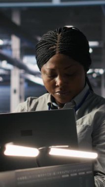 Veri merkezi meslektaşlarının yanındaki mutlu teknisyenin dikey video portresi yapay zeka tanılarını gözden geçiriyor. Neşeli bilişim uzmanı ve iş arkadaşları operasyonel kalabilmek için nöral ağ performansını analiz ediyorlar