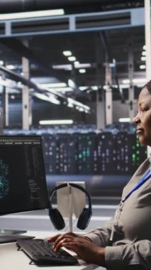 Yapay zeka görselleştirme sistemleri için yazılım güncellemeleri yaparak PC üzerinde dikey video veri merkezi programcısı kodlaması. Sunucu odasında yapay zeka kullanarak altyapıyı optimize eden Afrikalı Amerikalı bir kadın var.