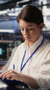 Sistem performans ölçümlerini değerlendirmek için uygulamaları takip eden dikey video sunucu odası yönetim panosu. Veri merkezi çalışanı bakım düzeltmeleri listesini inceliyor, tanılama çalışıyor