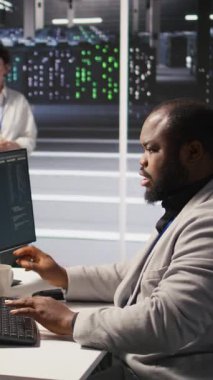 Veri merkezindeki dikey video stres teknisyeni yapay zeka sunucusu altyapısını yönetiyor, kahve içiyor. Yapay zekayı çalıştırmak için bilgisayar kullanan Afro-Amerikan işçiler, son teslim tarihiyle panikledi, kamera A