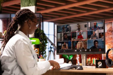 Ekip lideri, evdeki video görüşmeleri sırasında çalışanlarla konuşuyor. Evrakları inceliyor, iş vardiyalarını düzenliyor. Afrikalı Amerikalı denetçi çalışanlarla telekonferans yapıyor, belgeleri kontrol ediyor.