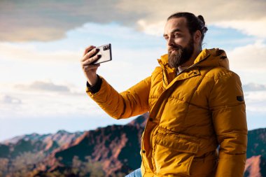 Azimli maceraperest panoramik dağ manzarasından zevk alır. Doğanın ve yükselen zirvelerin nefes kesici bir manzara yarattığı tepenin muhteşem arka planıyla selfie çeker..