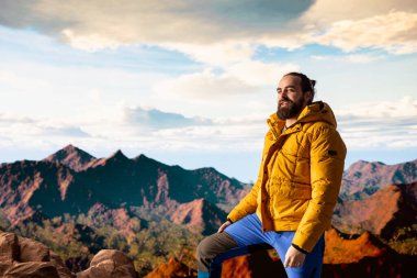 Kararlı dağcı dağların manzarasına hayran olmak için duraklıyor ve engin bir gökyüzü nefes kesici bir zemin oluşturuyor. Erkek yürüyüşçü doğa keşfi ve macerası için yürüyüş yapıyor..