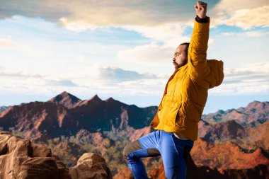 Mutlu maceracı dağın tepesinde olmanın heyecanını kucaklıyor, başarının gücünü hissediyor. Huzurlu gökyüzü ve uçsuz bucaksız vahşi doğayla ilham verici bir dağ sırası..