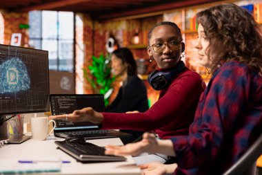 AI endüstrisinde hızlı teknolojik gelişmeler yapmak için beyin fırtınası yapan yazılım geliştiricileri. Afrikalı Amerikalı kadın ve iş arkadaşı kaldıraç makinası rekabetçi bir üstünlük kazanmak için teknoloji öğreniyor