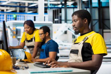 Ofisteki enerji kontrol sistemlerinde, güneş enerjisi imalatıyla çevrili Afrikalı Amerikalı denetleyici. Erkek mühendis fotovoltaik ve endüstriyel üretim hattını dengeliyor.