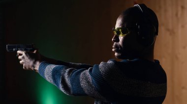 Güvenlik gözlüğü takan biri atış poligonunda ateşli silah talimi sırasında şarjör dolduruyor. Afrikalı Amerikalı adam silah dolduruyor, kendini savunmayı öğreniyor, silah doğrultuyor, kamera B
