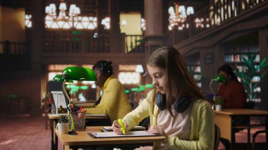 Öğrenim oturumu için önemli notları vurgulayan genç kız, ders kitabını tamamlamak ve üretken olmak için kütüphane veritabanından öğrenme materyalleri kullanıyor. Akademik başarı. Kamera A.