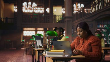 Sessiz bir kütüphane çalışma alanında dizüstü bilgisayarında yazı yazan mutlu kadın kütüphaneci, kendini kaynakları organize etmeye ve öğrencilere akademik yolculuklarında gurur ve uzmanlıkla rehberlik etmeye adamış. Kamera A.