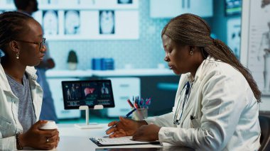 Bir hastayla tıbbi verileri inceleyen kadın pratisyen, sağlığa odaklı uzman istişare sırasında etkileşimi ve güveni teşvik eden. Afrikalı Amerikalı kız tavsiye istiyor. Kamera A.