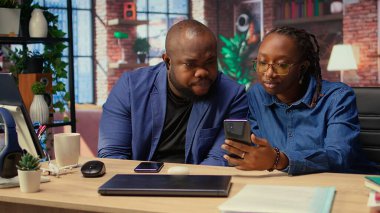 Genç siyahi çift kulaklıklarını paylaşıp akıllı telefondan Webinar dinliyor ve evdeki serbest işlerinde birlikte çalışıyorlar. Erkek ve kadın bir iş projesi hakkında tartışıyorlar. Kamera A.