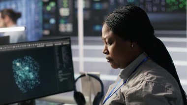 Veri merkezi sistem yöneticisi PC kullanarak nöral ağ yapay zeka görüntülemesini izliyor. Sunucu odasında Afrika kökenli Amerikalı bir kadın bilgisayarla donanımlı makine öğrenme işlemlerini denetliyor. Kamera A