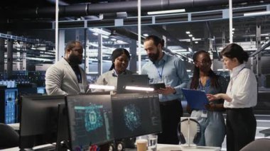 Sunucu odasında gülümseyen mühendislik ekibi altyapı tanılarını inceliyor. Veri merkezinde çalışan bilişim uzmanları, sistem bütünlüğünü ve çalışma saatlerini korumak için performans verilerini analiz ediyorlar. Kamera A