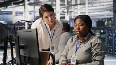 Veri merkezi ekip lideri ve bilişim uzmanı yapay zeka ekipmanlarının performans gösterge panellerini inceliyor. Sunucu odası yöneticisi sistem yöneticisiyle ilgilenir. Ekranda inceleme makinesi öğrenme algoritmaları, kamera A