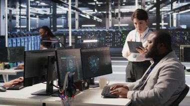 Sunucu odası yöneticisi, derin öğrenme algoritmalarını inceleyen teknisyenleri denetliyor. Veri Merkezi ekip lideri ve Afro-Amerikan çalışan denetimi Yapay Zeka ekipman platformlarının performans göstergesi, kamera A