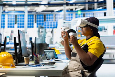 Siyah teknisyen, yenilenebilir enerji üretim endüstrisinde çalışmak için dijital yazılım kullanarak VR gözlükleri üzerinde çoklu güneş paneli tasarımlarını test ediyor. Üretim hattını optimize eden kadın mühendis.