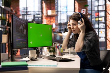 Yeşil ekranın yanında bir film montajı yapan kadın kameraman, çift taraflı monitör kurulumu ve düzenleme yazılımı ile birden fazla iş yapıyor. Sinema endüstrisi için üretim sonrası görevler bitiriliyor.