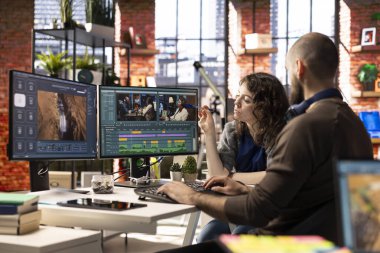 Erkek ve kadın film yapımcıları, yaratıcı bir video projesi için modern bir teknoloji kurulumu ve kurgu yazılımı kullanarak, post prodüksiyon için bir video çekimi düzenliyorlar. Çift monitörlü modern çalışma alanı.