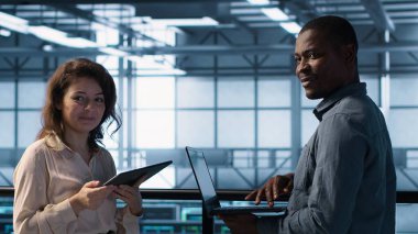 Veri merkezinde dizüstü bilgisayar kullanan gülümseyen yöneticiler, sunucu viralizasyonunu yönetiyorlar. Neşeli bilişim uzmanı ve Afro-Amerikan adam sunucu odasında not defteri kullanıyor, altyapı güvenilirliğini sağlıyorlar, kamera A